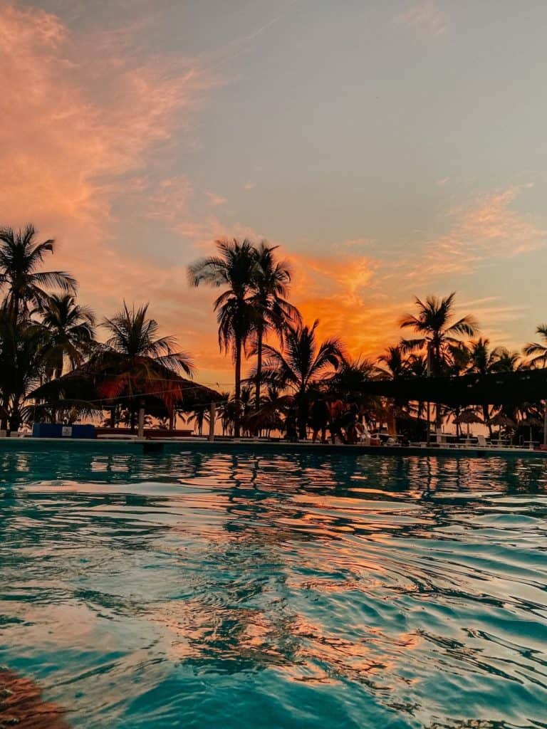 atardecer, palmas, y piscina en la playa