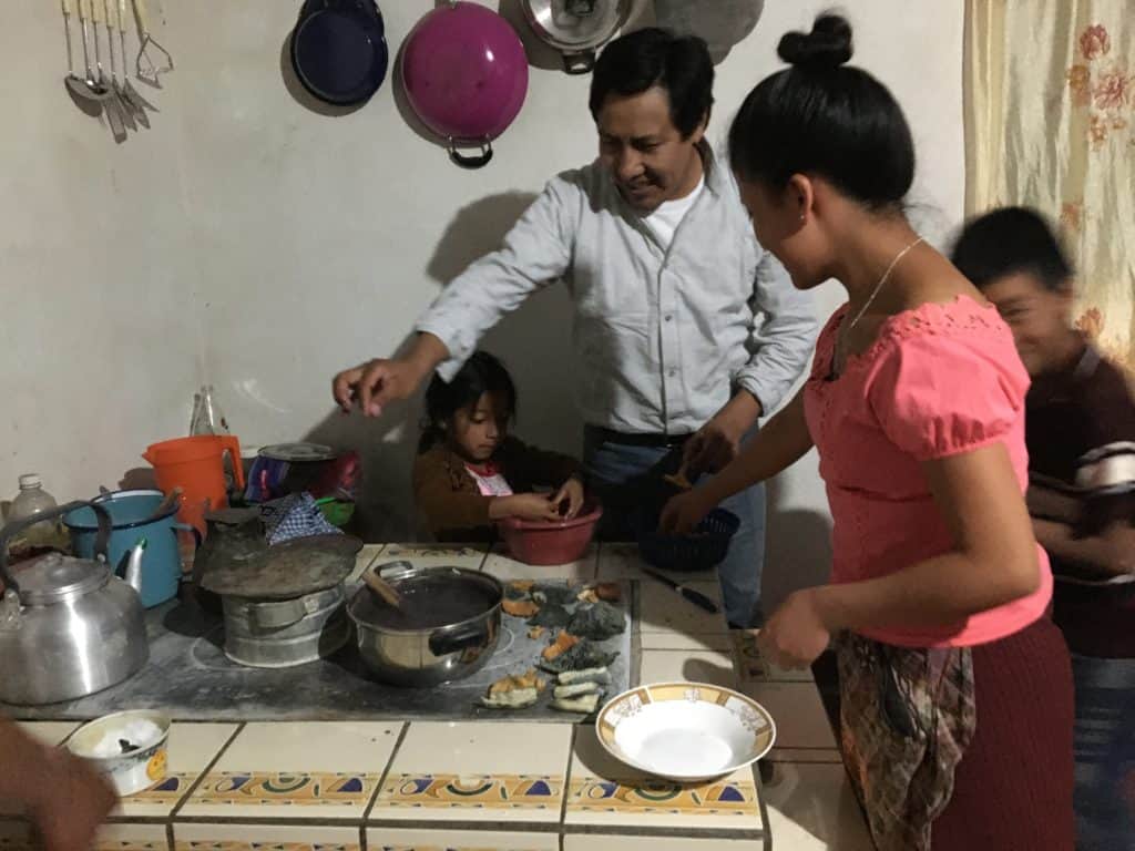 Man and children around a wood-fired stove cooking beans and mushrooms