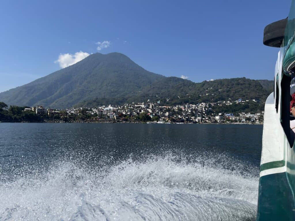 Water spashes from the side of a boat as it heads across a lake toward a beautiful volcano
