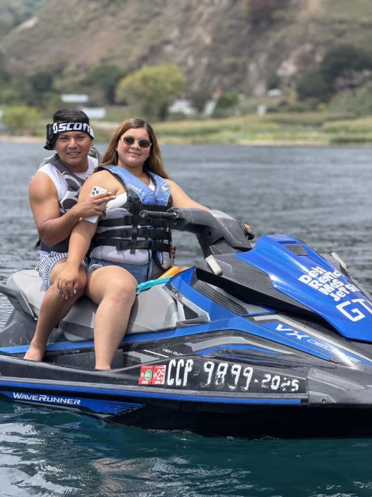 A couple on a jetski on Lake Atitlán smile at the camera.