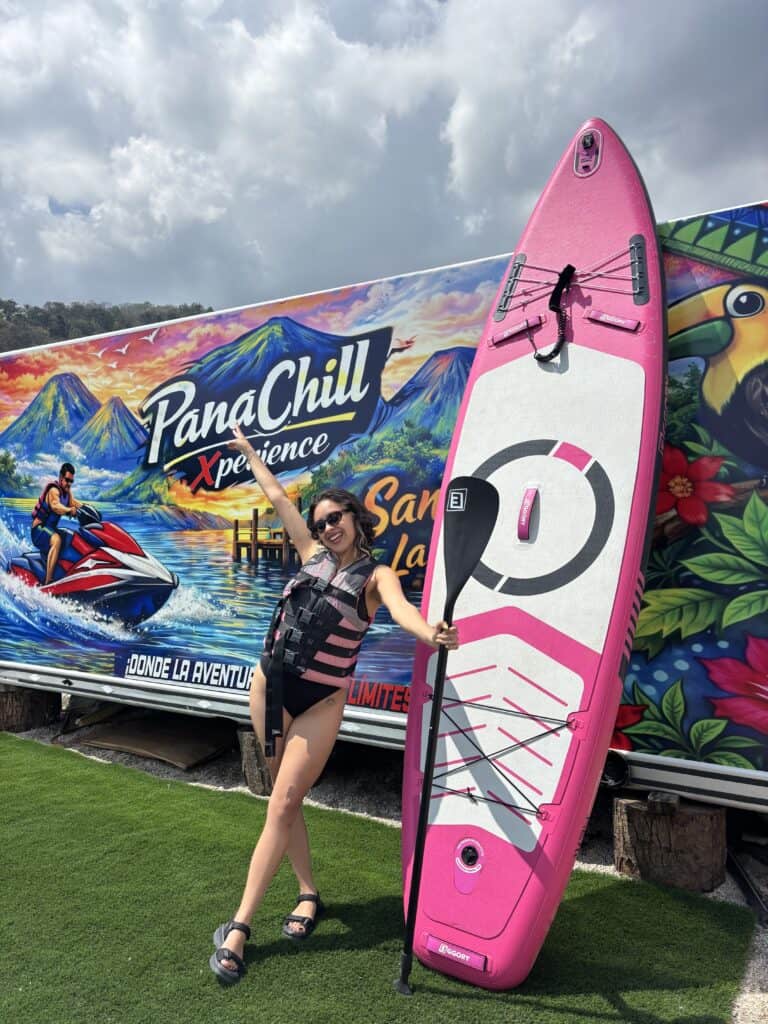 A woman standing next to a pink paddleboard thrusts her hand into the air exuberantly