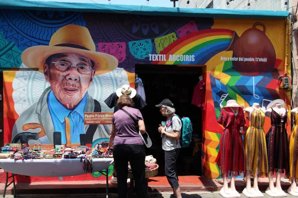 Two women shop outside a textile store painted with a colorful mural of a local man.