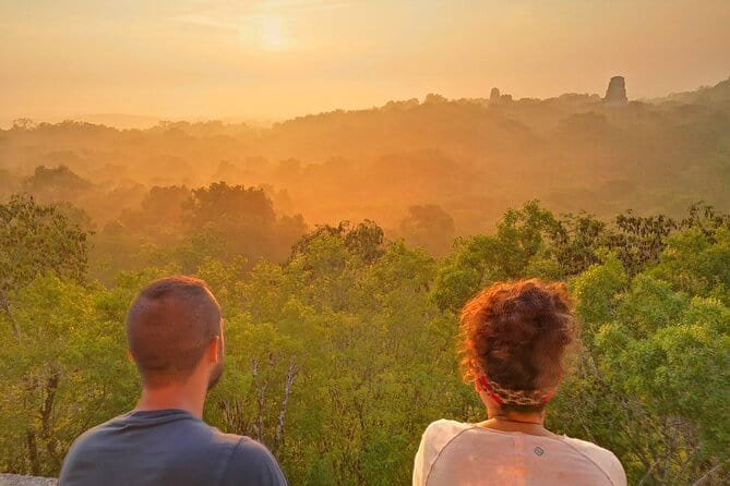 Two tourists look out over a jungle bathed in golden light