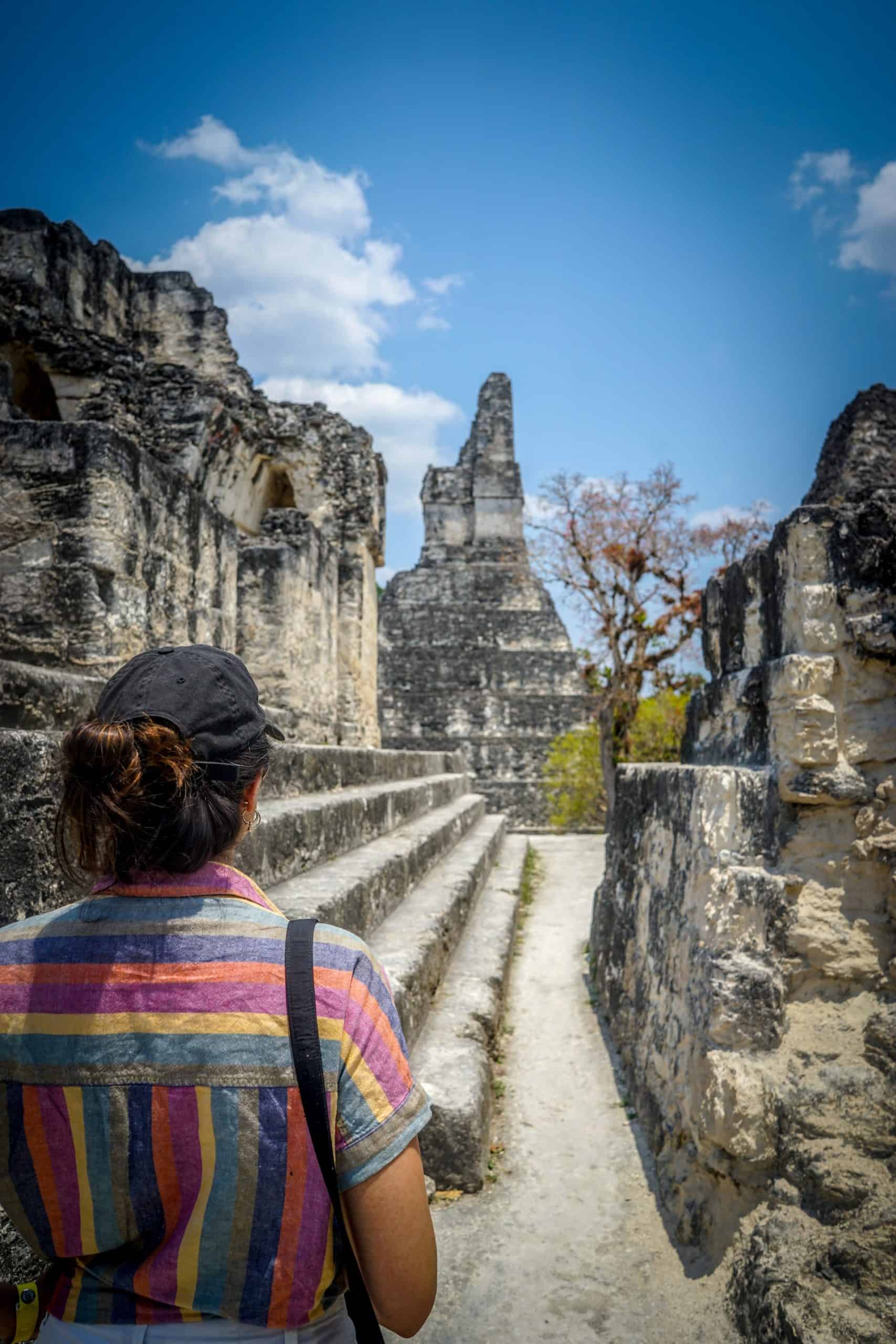 Tours a Tikal desde Flores - Mujer mirando el Templo del Gran Jaguar desde detrás de otras ruinas en el Parque Nacional de Tikal