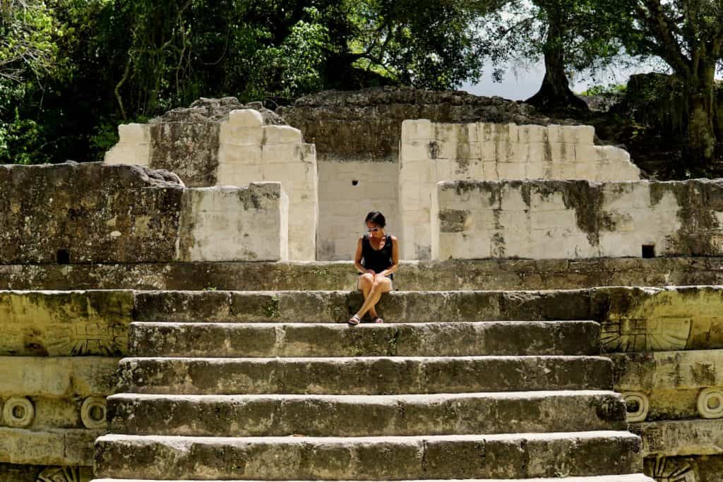 A woman sits on the steps of Mayan ruins in Tikal National Park
