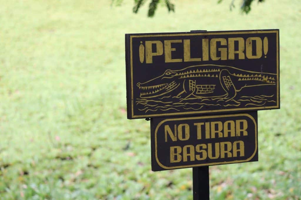 A sign with a drawing of an alligator says "Danger, don't throw trash" in Tikal National Park, Petén, Guatemala. Tourists have a blast on Tikal tours from Flores.